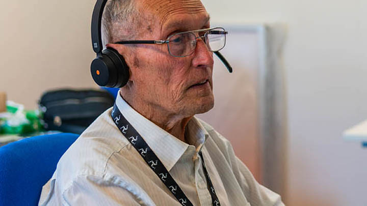 Healthcare volunteer using computer An older man with glasses wearing a headset.