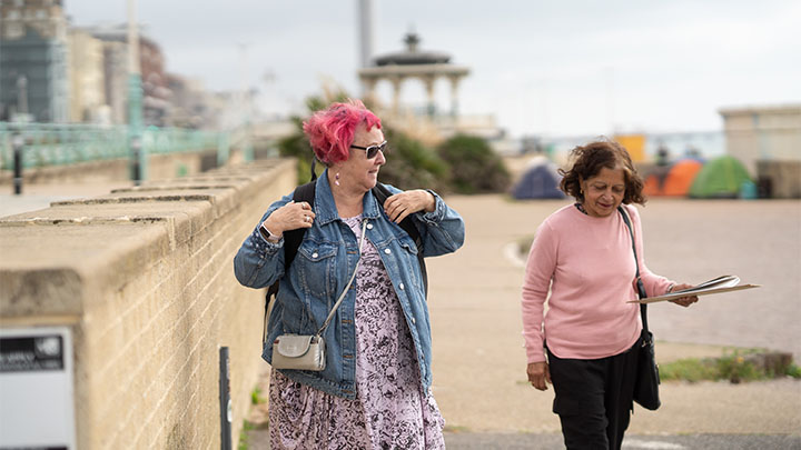 Two women smiling and walking along seafront. Two women smiling and walking along seafront.