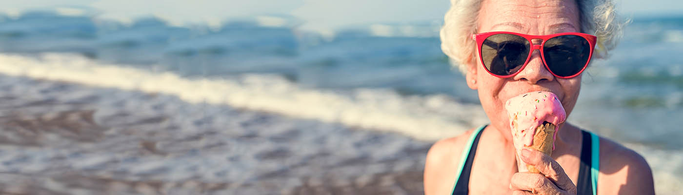 An older lady eating ice-cream at the beach.