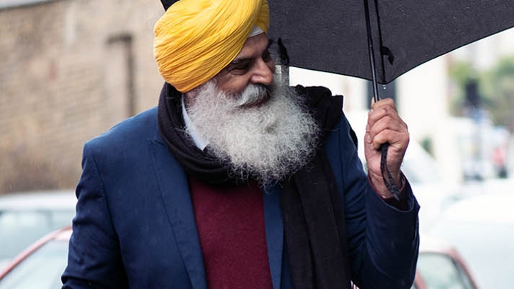 An older Asian man wearing a turban and holding an umbrella.